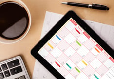 Workplace with tablet pc showing calendar and a cup of coffee on a wooden work table close-up